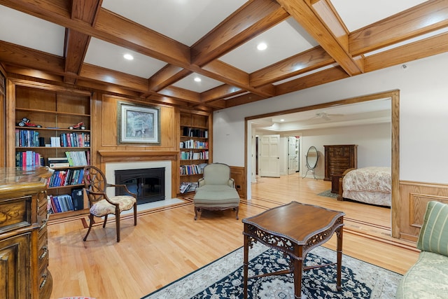 living area with beam ceiling, wood finished floors, a glass covered fireplace, built in shelves, and coffered ceiling