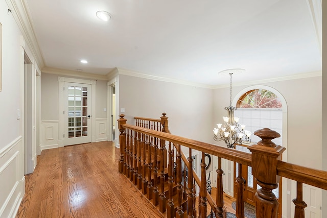 hallway with an upstairs landing, a chandelier, light wood-type flooring, crown molding, and a wainscoted wall