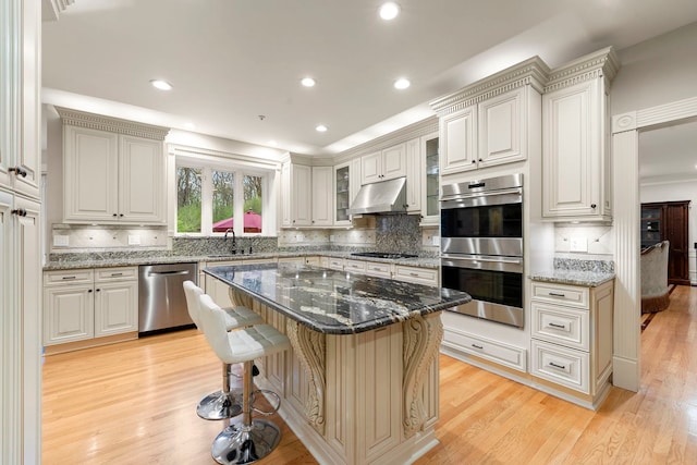 kitchen featuring appliances with stainless steel finishes, a sink, a breakfast bar, under cabinet range hood, and backsplash