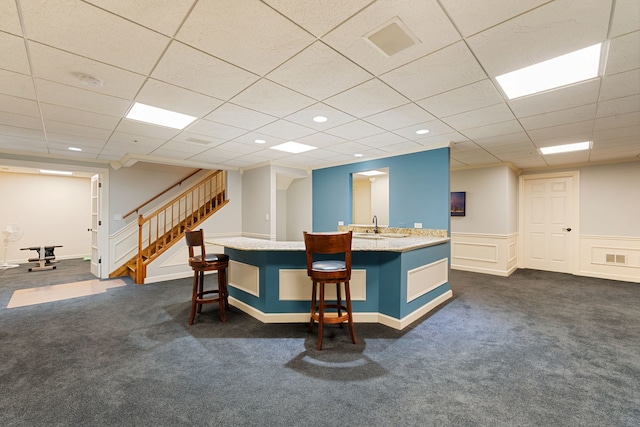 kitchen featuring dark colored carpet, a sink, a kitchen bar, an island with sink, and light stone counters