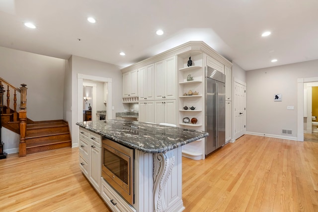 kitchen with built in appliances, open shelves, light wood-style flooring, dark stone counters, and recessed lighting