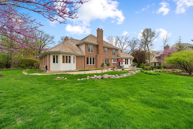 back of house with a chimney, brick siding, a patio area, and a lawn