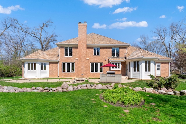 rear view of property featuring a chimney, brick siding, exterior kitchen, a yard, and a patio area