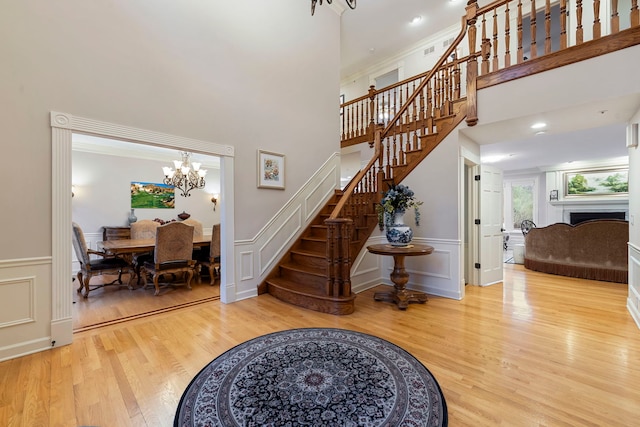 stairs with a chandelier, wood finished floors, a decorative wall, wainscoting, and a towering ceiling