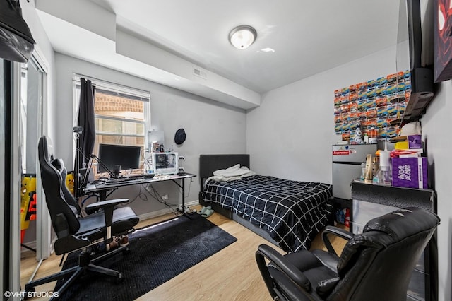 bedroom with baseboards, freestanding refrigerator, wood finished floors, and visible vents
