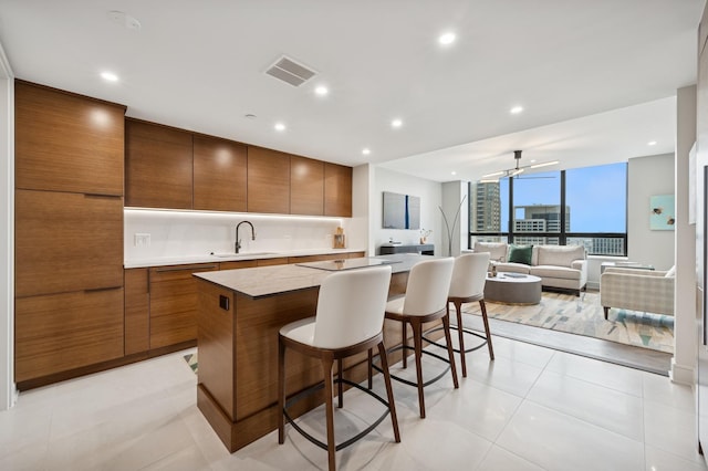 kitchen featuring a breakfast bar area, visible vents, a center island, brown cabinets, and a sink