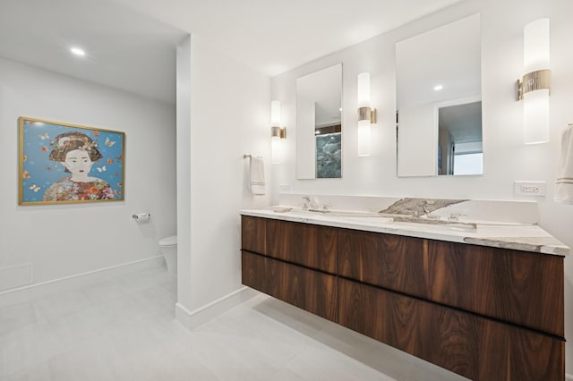 full bathroom featuring double vanity, toilet, baseboards, and a sink