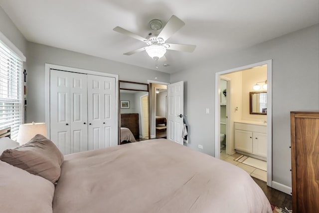 bedroom featuring a closet, a ceiling fan, baseboards, ensuite bath, and wood finished floors