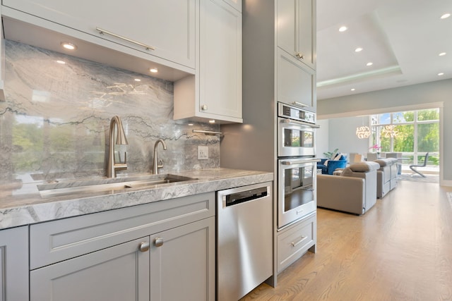 kitchen with recessed lighting, a sink, light wood finished floors, backsplash, and stainless steel appliances
