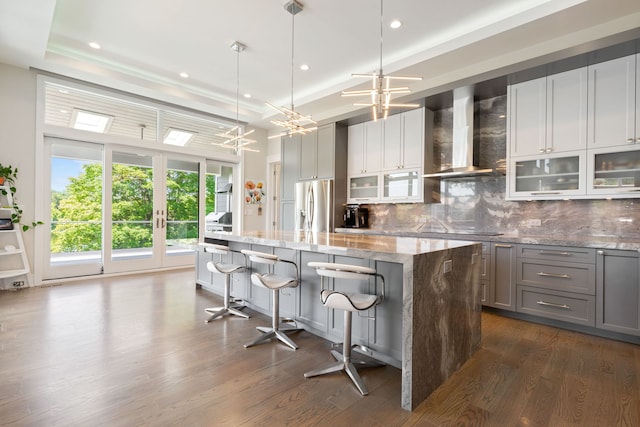 kitchen featuring a kitchen island, wall chimney range hood, stainless steel refrigerator with ice dispenser, gray cabinets, and black electric cooktop