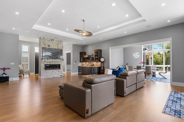 living room featuring recessed lighting, a raised ceiling, bar, a large fireplace, and light wood-style flooring