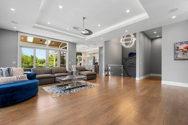 living room with recessed lighting, baseboards, a raised ceiling, and wood finished floors