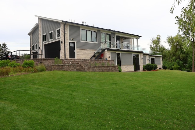 back of house featuring stairs, an attached garage, stone siding, a balcony, and a lawn