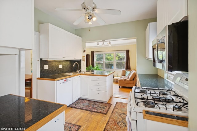 kitchen featuring a sink, a peninsula, white appliances, and white cabinetry