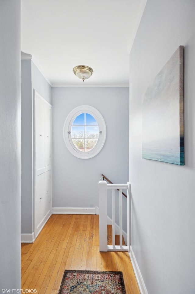 hallway featuring baseboards, ornamental molding, an upstairs landing, and hardwood / wood-style flooring