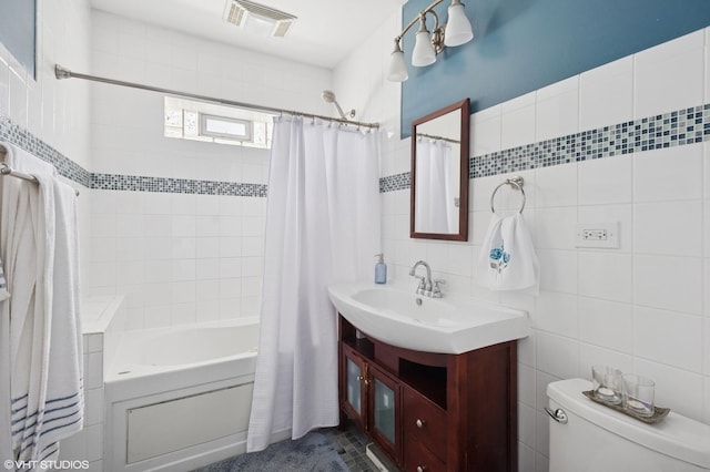 full bath with visible vents, vanity, toilet, tile walls, and shower / bath combo