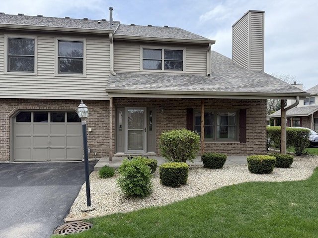 view of property featuring driveway, a chimney, a garage, brick siding, and a shingled roof