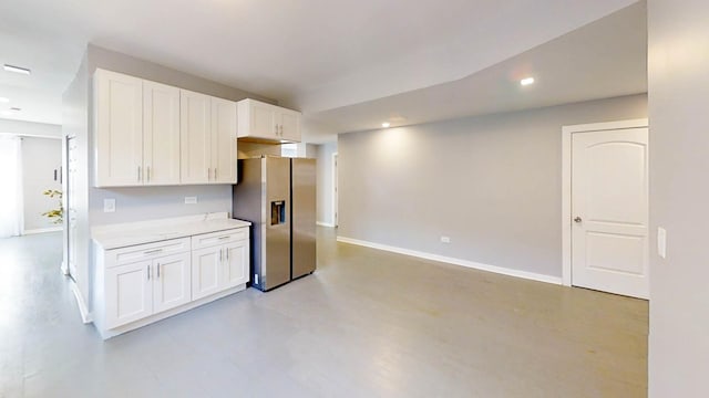 kitchen featuring recessed lighting, baseboards, stainless steel fridge, light countertops, and white cabinets