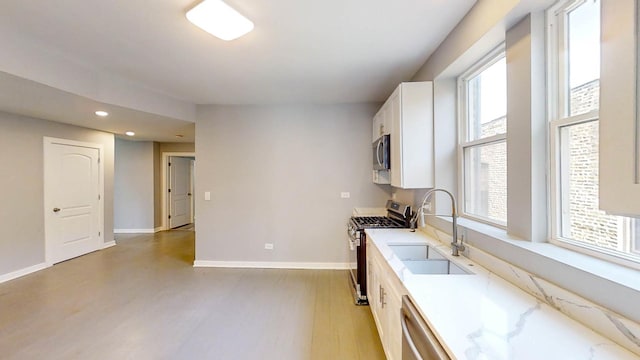 kitchen with baseboards, light wood finished floors, a sink, white cabinetry, and stainless steel appliances