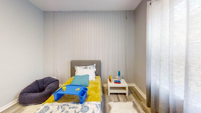 bedroom featuring an accent wall, wooden walls, baseboards, and wood finished floors