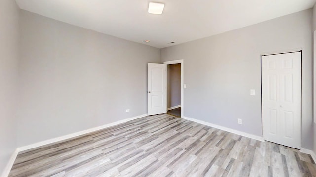 unfurnished bedroom with baseboards, light wood finished floors, and a closet