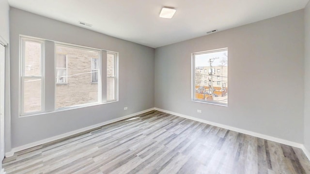 spare room with baseboards, a healthy amount of sunlight, visible vents, and wood finished floors
