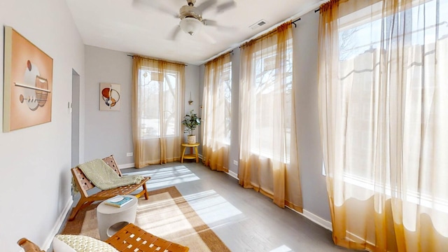 sitting room featuring a wealth of natural light, visible vents, baseboards, and ceiling fan