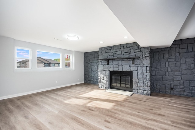 unfurnished living room with a stone fireplace, baseboards, and wood finished floors