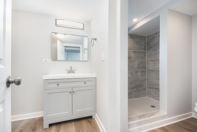full bath featuring baseboards, wood finished floors, a tile shower, and vanity