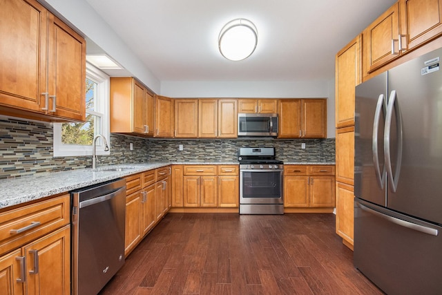 kitchen featuring light stone countertops, a sink, stainless steel appliances, backsplash, and dark wood-style floors