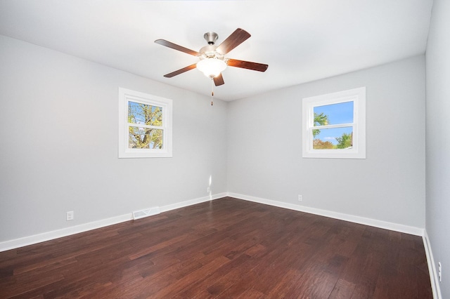 empty room featuring baseboards, dark wood-type flooring, and a wealth of natural light