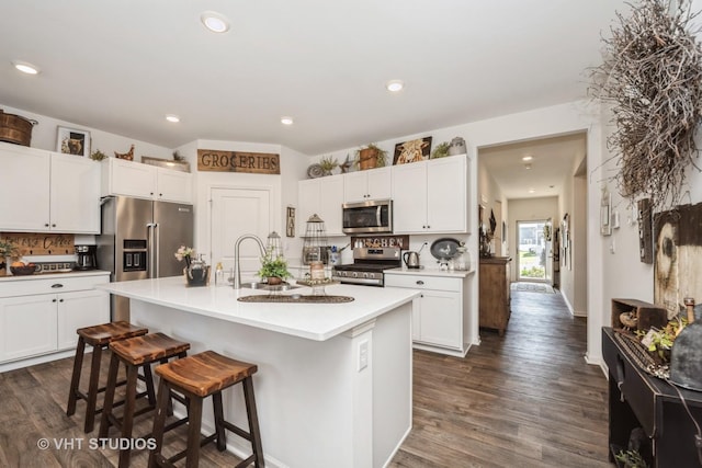 kitchen with appliances with stainless steel finishes, a breakfast bar, a sink, white cabinets, and recessed lighting