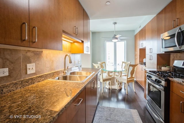 kitchen with a ceiling fan, dark wood-style flooring, brown cabinets, a sink, and stainless steel appliances