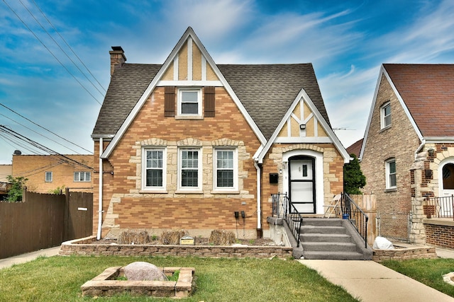 3214 N Rutherford Ave, Chicago, IL 60634 - tudor-style house featuring a chimney, a front yard, brick siding, fence, and a shingled roof
