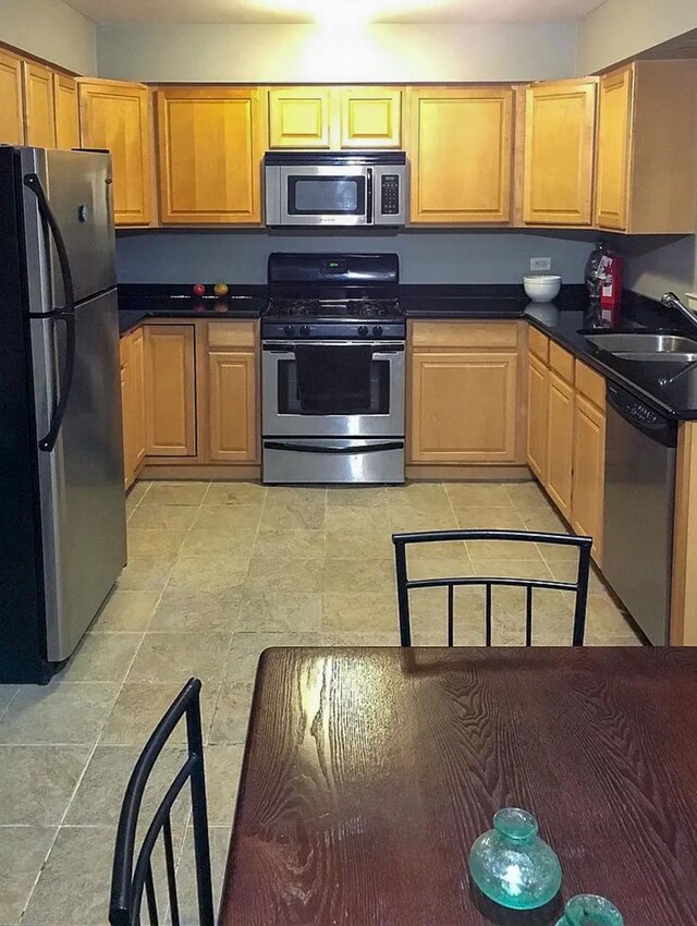 kitchen featuring appliances with stainless steel finishes, a sink, dark countertops, and light tile patterned floors