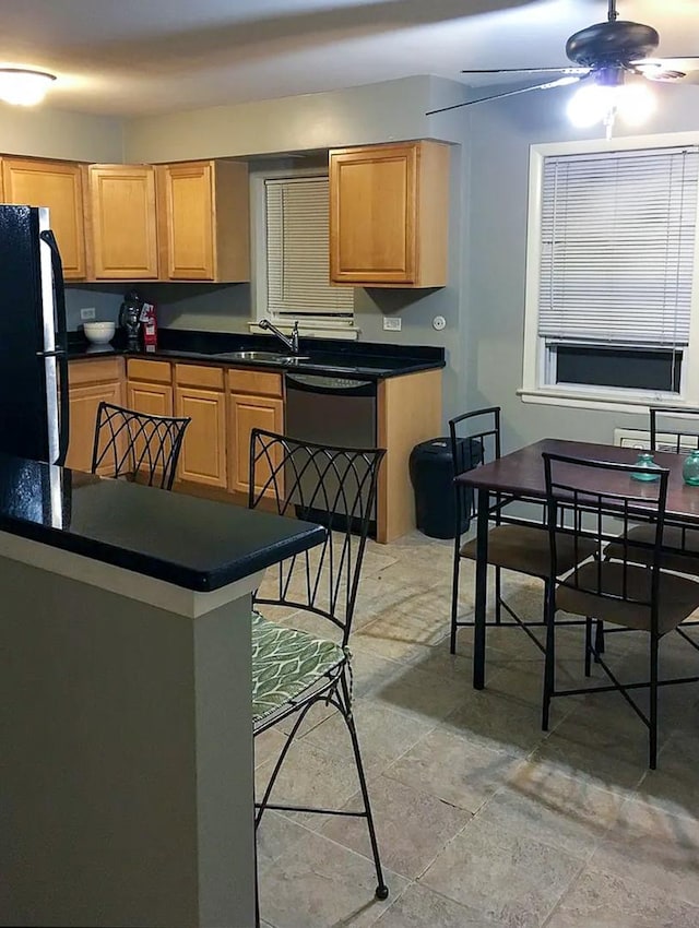 kitchen featuring dark countertops, black appliances, ceiling fan, a sink, and light brown cabinets