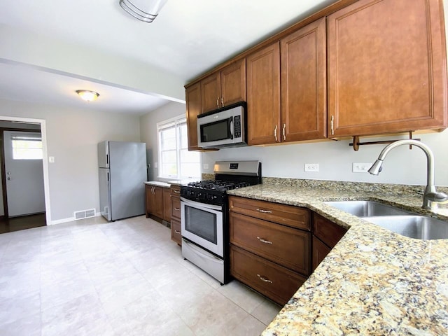 kitchen featuring visible vents, brown cabinetry, light stone countertops, a sink, and stainless steel appliances