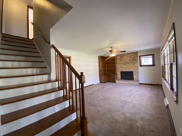 unfurnished living room featuring ceiling fan, a fireplace, stairway, baseboards, and carpet