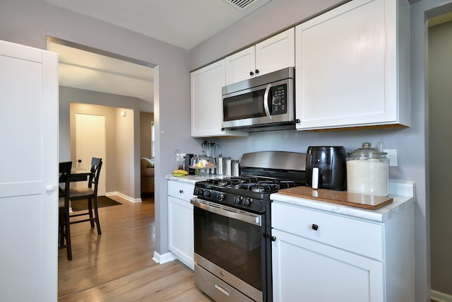 kitchen featuring light countertops, stainless steel appliances, light wood-style flooring, and white cabinetry