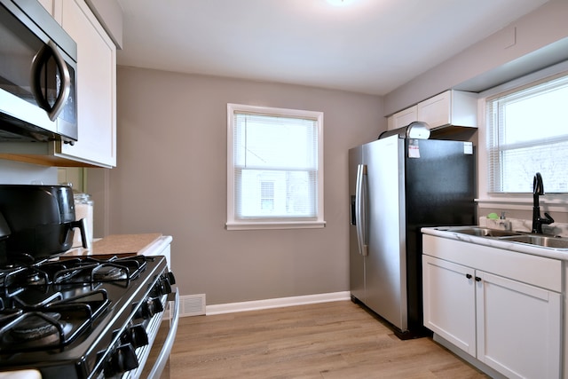 kitchen with visible vents, appliances with stainless steel finishes, a sink, white cabinets, and light wood finished floors