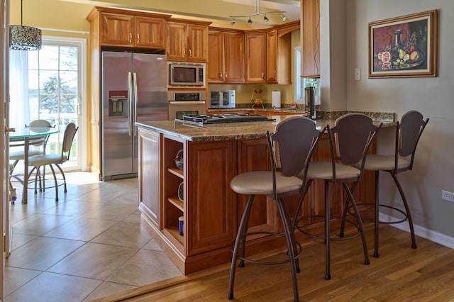 24270 N Forest Dr, Lake Zurich, IL 60047 - kitchen featuring stainless steel appliances, dark stone counters, brown cabinets, a peninsula, and open shelves
