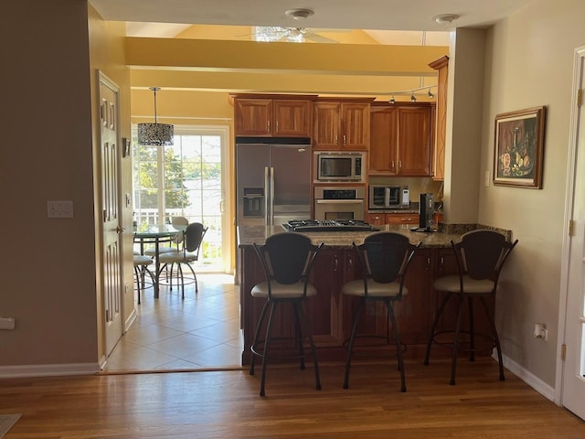 24270 N Forest Dr, Lake Zurich, IL 60047 - kitchen with stainless steel appliances, brown cabinetry, a peninsula, baseboards, and a breakfast bar area