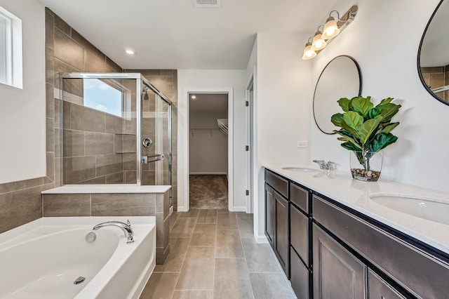 full bath featuring double vanity, a walk in closet, a bath, a stall shower, and a sink