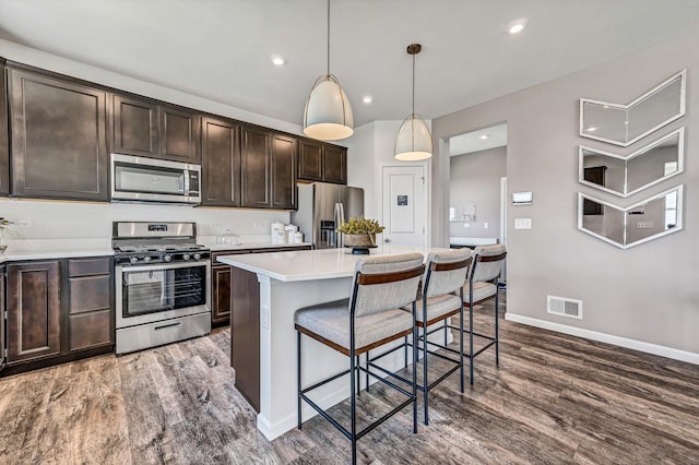 kitchen with dark brown cabinets, a breakfast bar, stainless steel appliances, wood finished floors, and visible vents