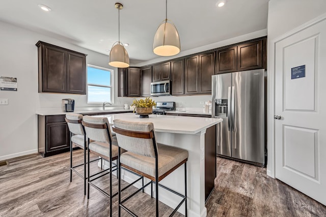 kitchen featuring light wood finished floors, a kitchen breakfast bar, dark brown cabinetry, and stainless steel appliances