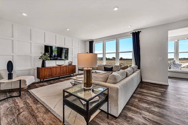 living room featuring baseboards, a decorative wall, recessed lighting, and dark wood-type flooring