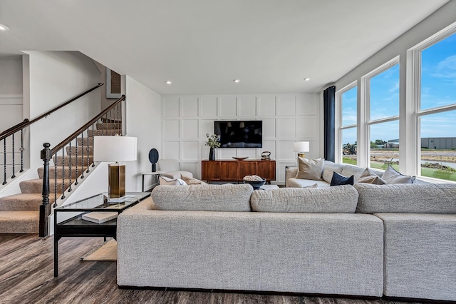 living area with recessed lighting, dark wood finished floors, a decorative wall, and stairs