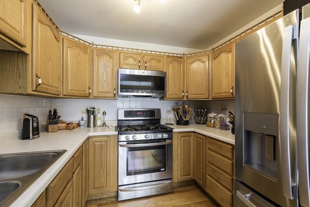 kitchen with light countertops, backsplash, stainless steel appliances, and light wood-style flooring