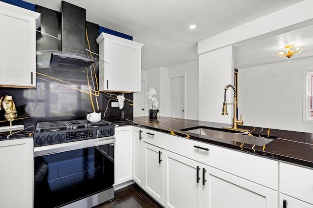 kitchen featuring decorative backsplash, wall chimney range hood, white cabinetry, range with gas cooktop, and a sink