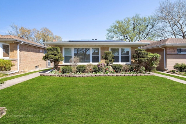ranch-style home featuring roof mounted solar panels, brick siding, and a front yard